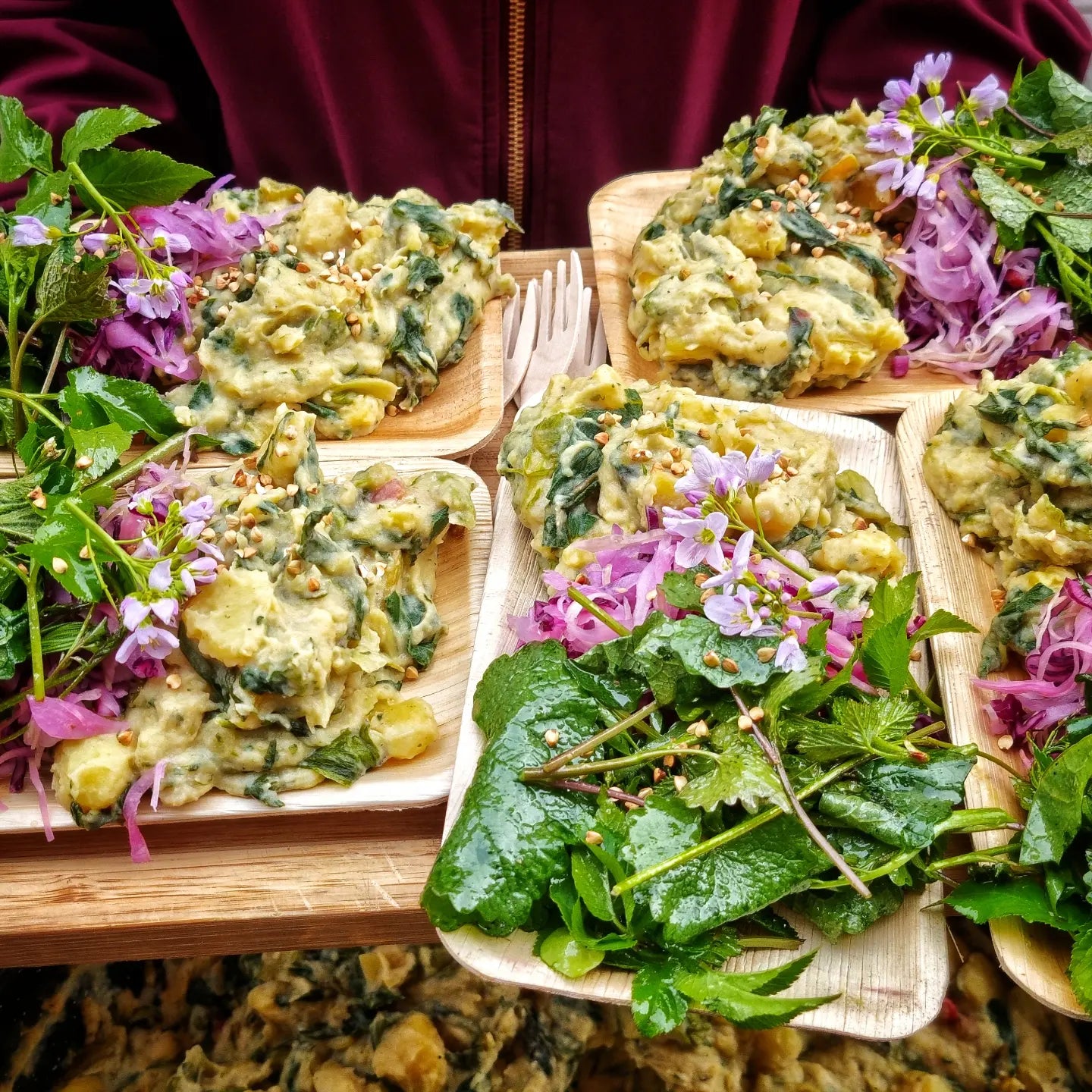 Mehrere Teller eines Gerichts mit Kartoffeln, Wildkräutern und Krautsalat