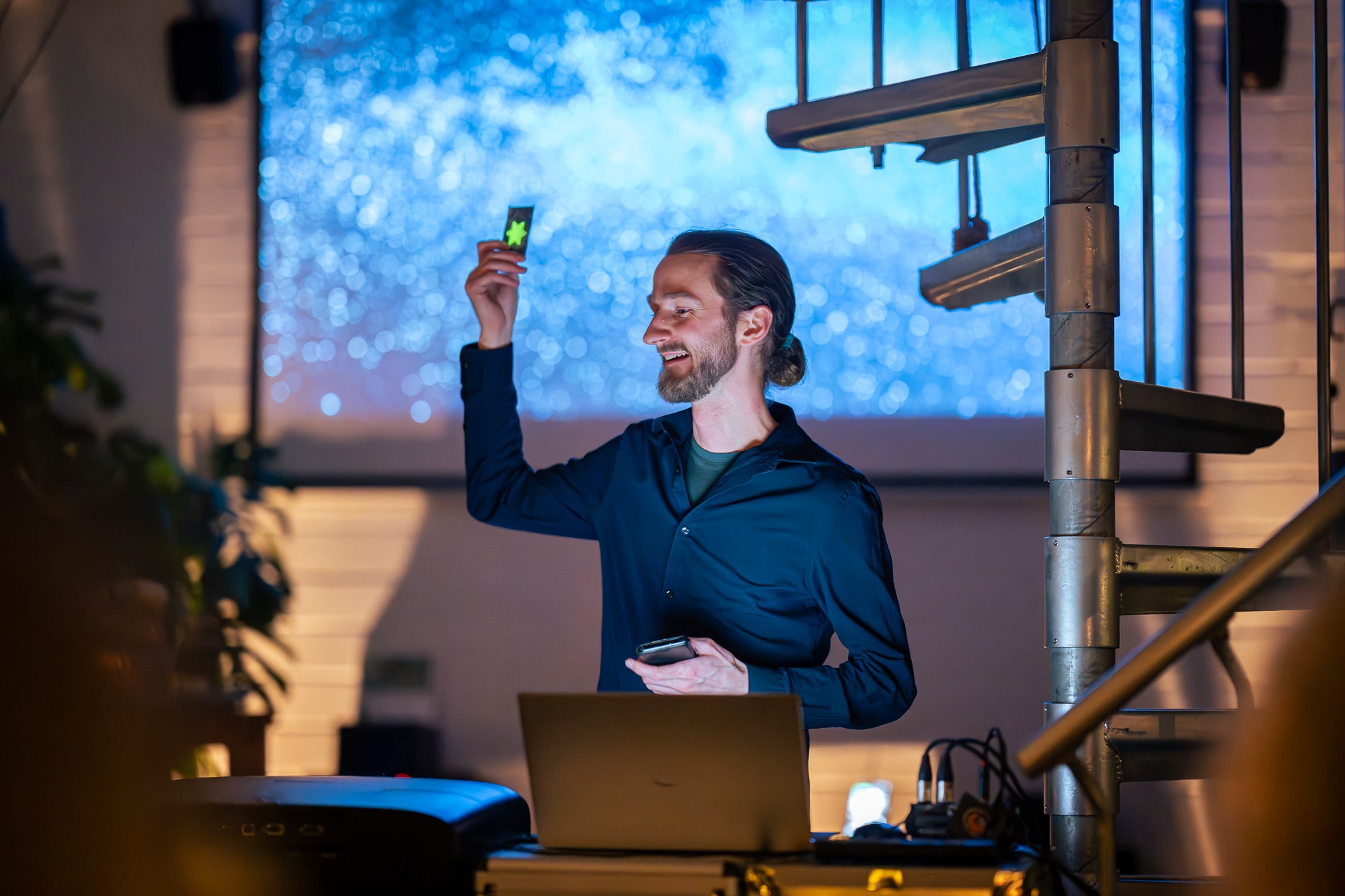 Sebastian Worm vor einer Leinwand beim Vortrag. Man sieht eine Wendeltreppe, einen Laptop und weitere Technik.
Bildrecht bei Thomas Mohn.