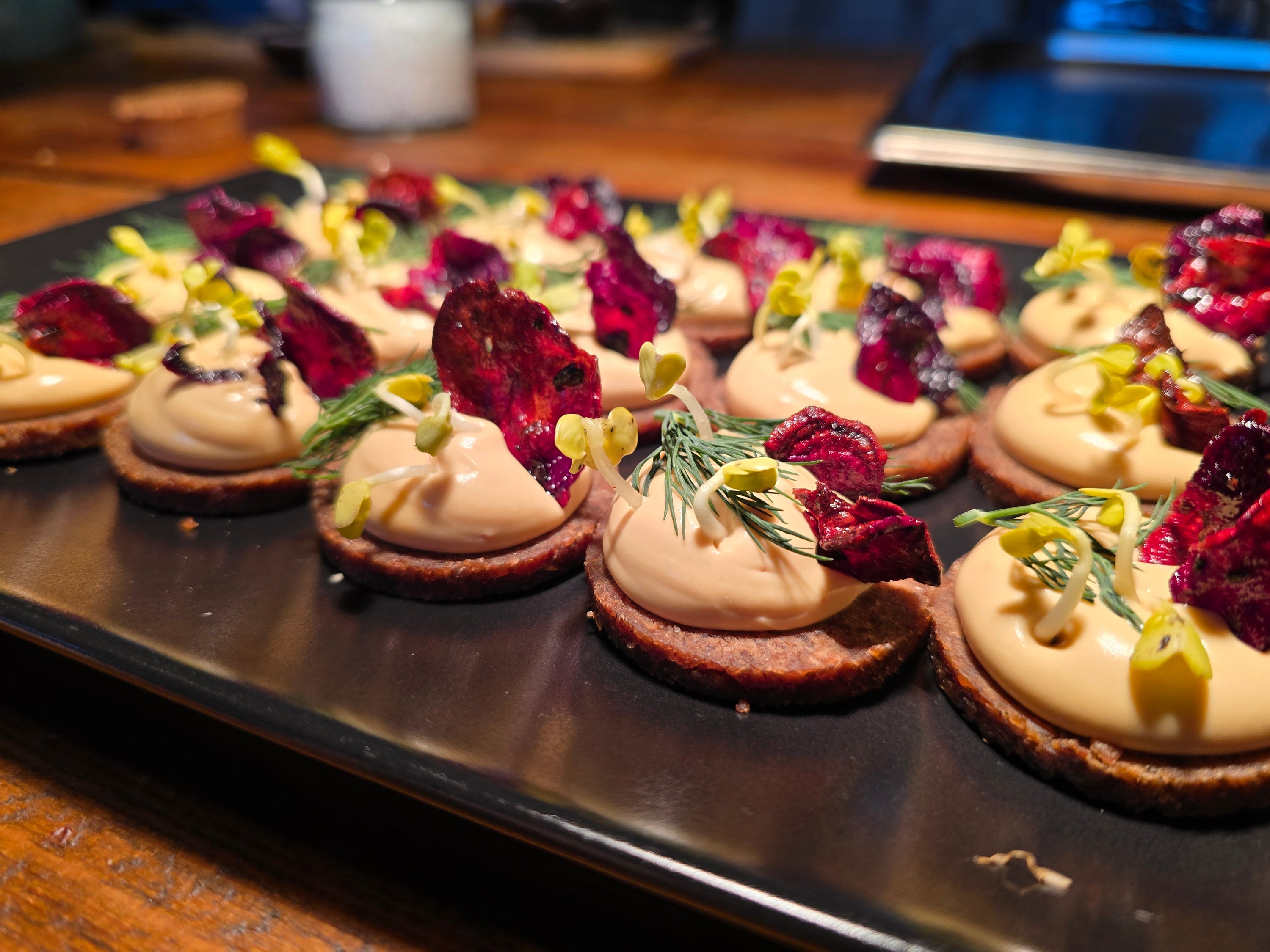 Ein Teller mit Amuse Gueule. Man sieht Pumpernickel, eine Creme, Rote Bete, Dill und Kresse. 
