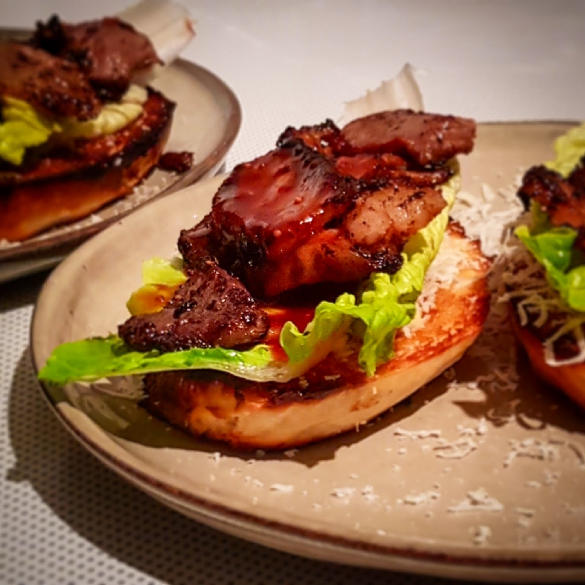 Offener Burger auf einem Teller. Belag aus Romasalat und mariniertem Fleisch. 