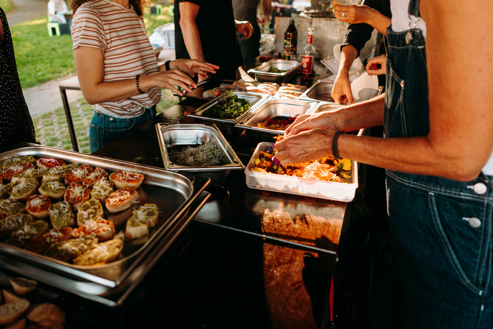 Foodbike - Fahrradcatering in Münster – mehrere Menschen kochen gemeinsam und bereiten Essen zu. man sieht 9 Hände und mehrere GN-Behäöter mit Essen und Saaten und Salaten.