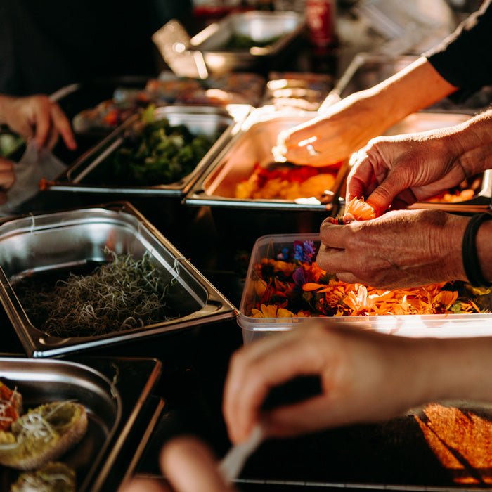 Foodbike in Münster - Catering Outdoor – mehrere Hände bereiten Essen, wie Blüten und Gewürze, wie auch Möhren und Gurken vor. Die unterschiedlichen Komponenten stehen in GN-Behältern