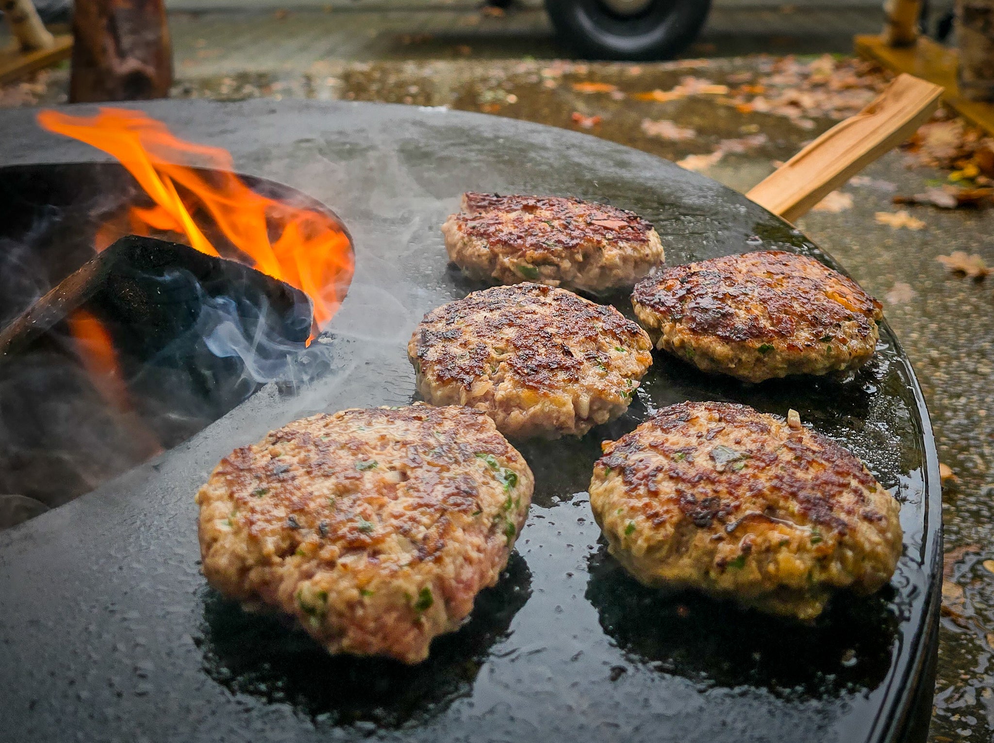 Fleischpattys am Lagerfeuer auf einer Grillplatte.