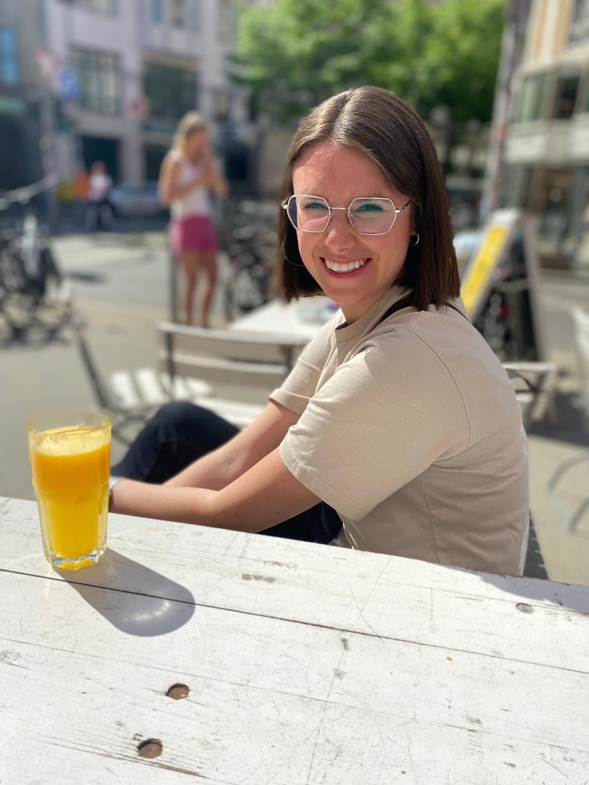 Eventlocation in Münster - Bewertung einer lächelnden Frau mit Brille, Ende 20, mit dunklen Haaren, an einem Tisch sitzend