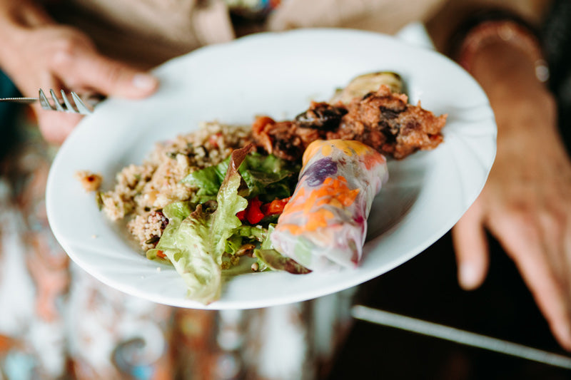 Catering in Münster - gesundes Essen wie Salat, Reis, Zucchini und Summerrollauf einem weißen Teller, der von einer Hand gehalten wird