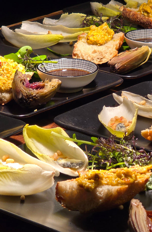 Catering in Münster - Events – mehrere schwarze große Eckige Teller mit unterschiedlichen Salat und Artischocke, wie auch einer kleinen Schüssel mit Suppe. 