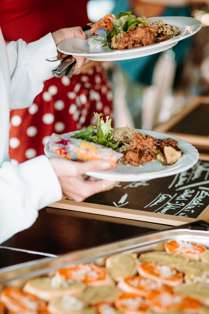 Catering in Münster und Münsterland – eine Person hält zwei Teller mit Salat, Reis, Aubergine und Zucchini, wie auch Besteck. in der Ecke sieht man einen GN-Behälter mit noch mehr gesundem Essen.