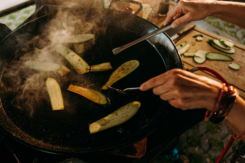 Foodbike Münster - Showcooking - Fahrrad Catering – Hände braten in einer Pfanne, welche dampft Aubergine und Zucchinistreifen an